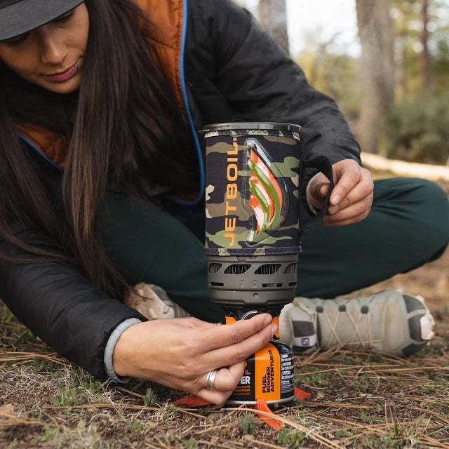 A Jetboil Flash 1.0L cooking system set up on a wooden log with only a fuel canister and a lightweight camping mug nearby, highlighting its efficiency for minimalist camping.