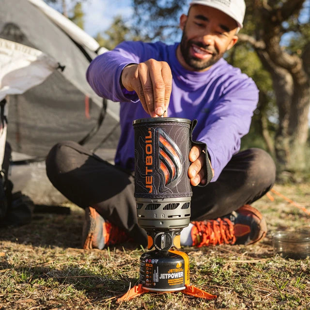 The Jetboil Flash Java 1.0L cooking system on a campsite table, alongside the silicone coffee press, a JetPower fuel canister, and a camping mug, creating the perfect morning coffee setup.