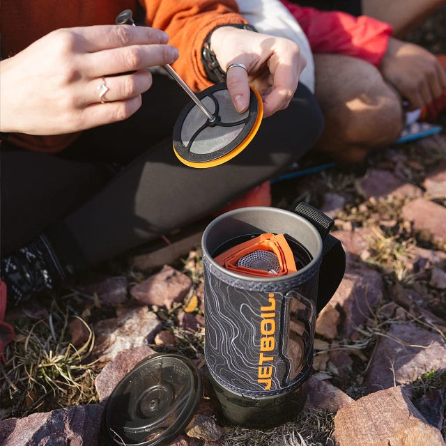 The Jetboil Flash Java 1.0L displayed with compatible accessories like the Hanging Kit 2.0, Pot Support 2.0, Summit Skillet, and 1.5L Ceramic Cook Pot, showing its versatility for outdoor cooking.