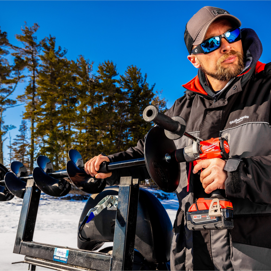 Person holding a drill and ice fishing equipment in a snowy outdoor setting