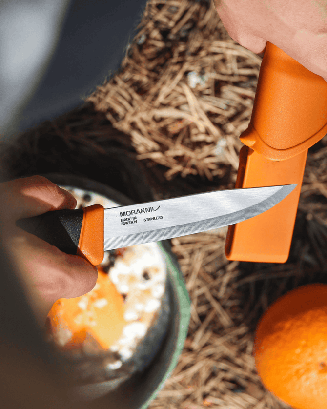 Orange Morakniv knife being used on an orange with a natural background
