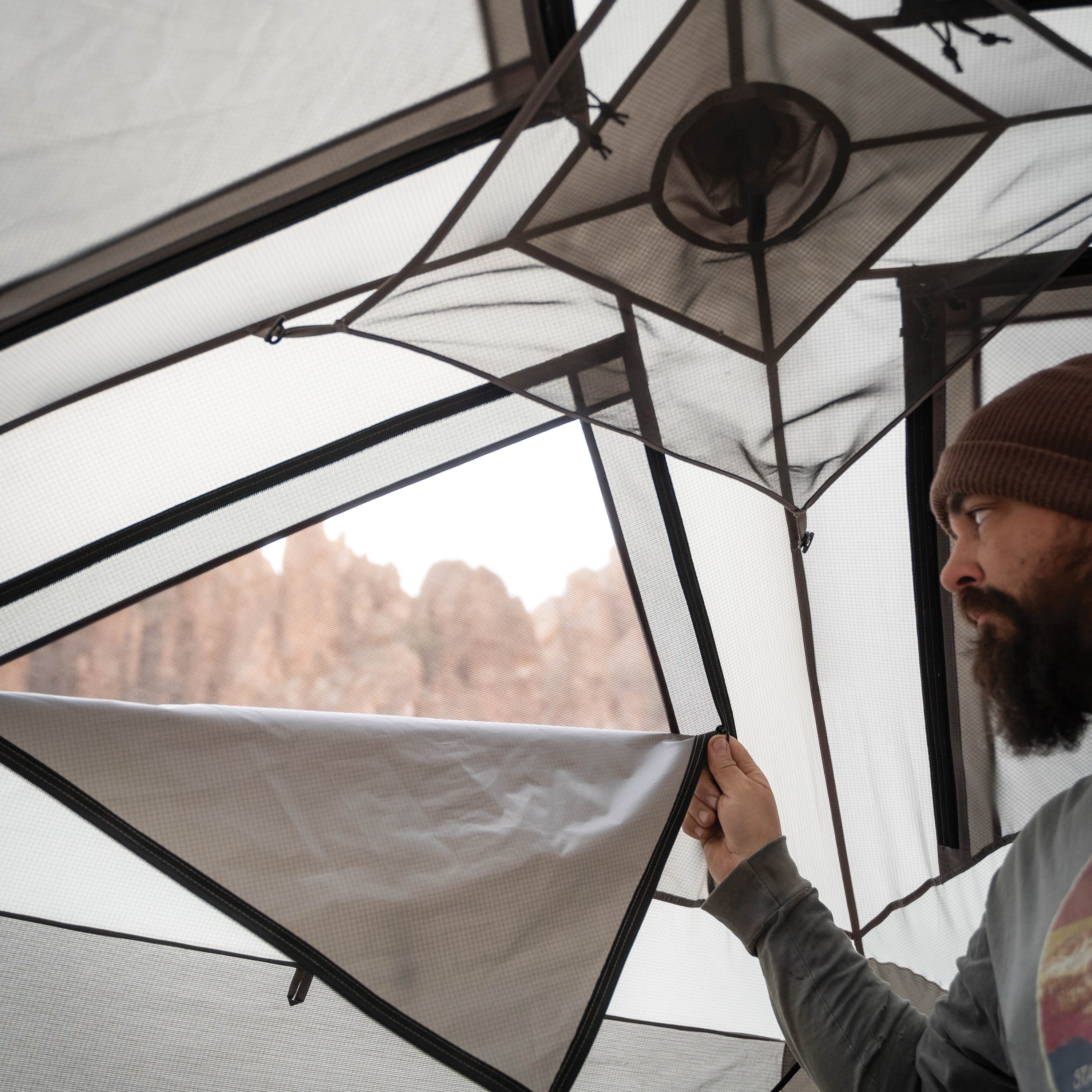 Person adjusting a tent with a scenic view outside