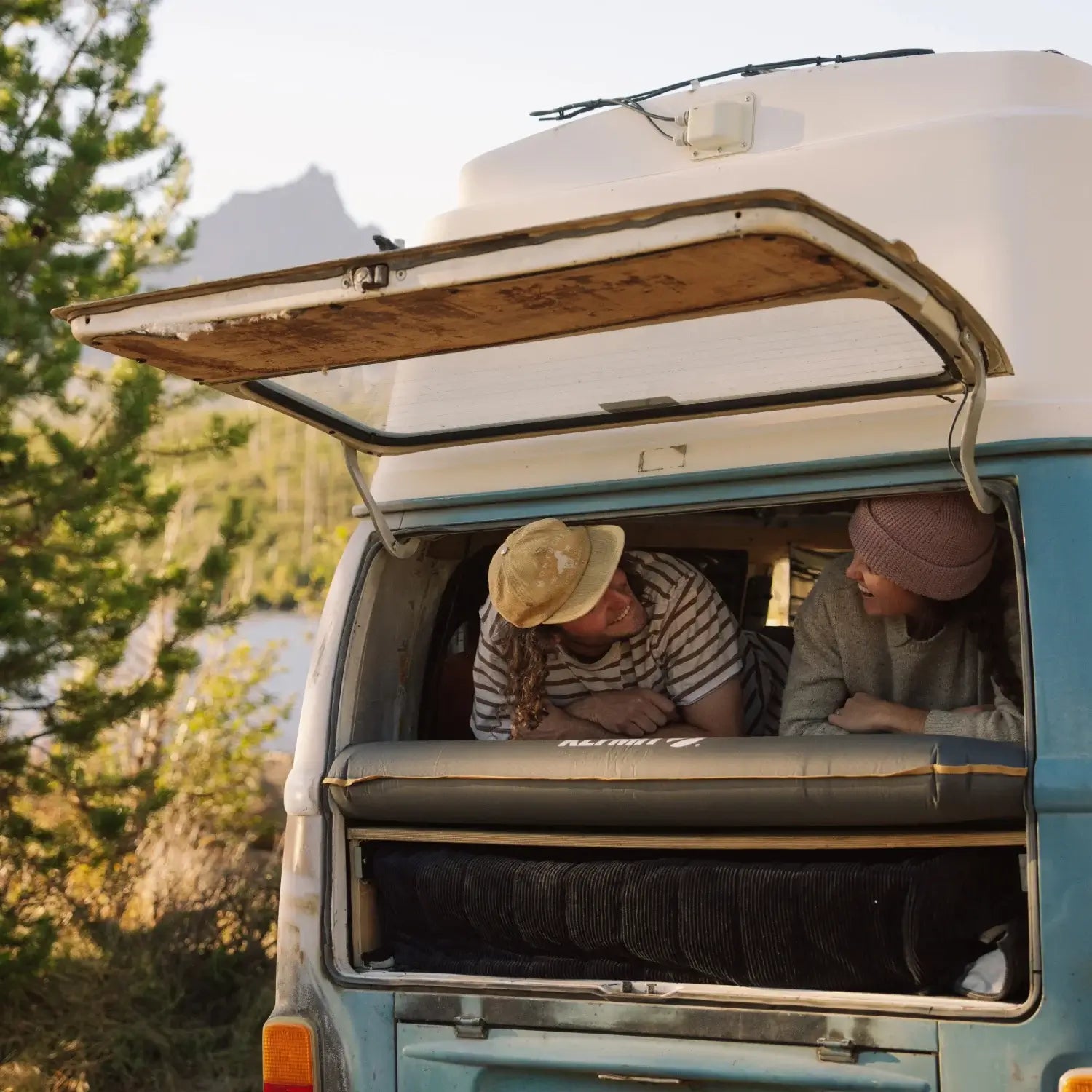 Two people sitting inside a van with an open roof, surrounded by nature.
