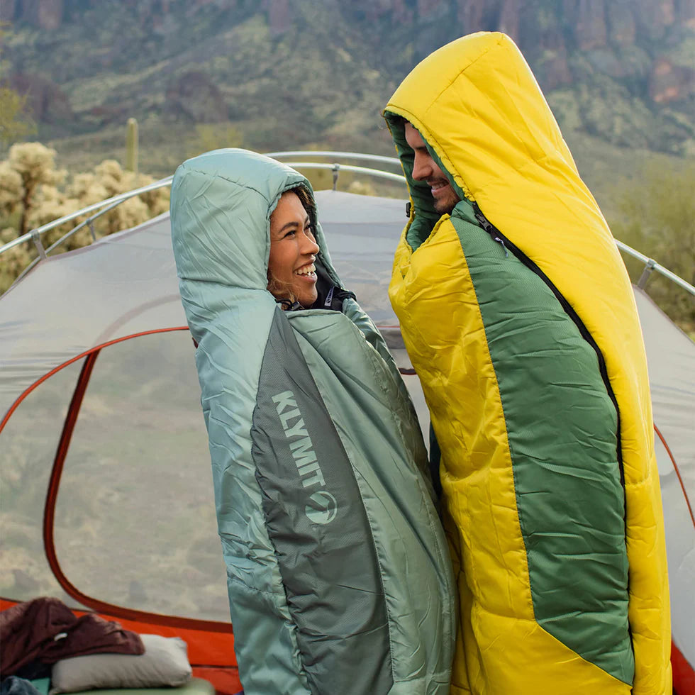 Sleeping Bag in Use: A person sleeping inside the Wild Aspen 20, bundled up with the hood adjusted, demonstrating its snug fit and insulation in a camping setting.