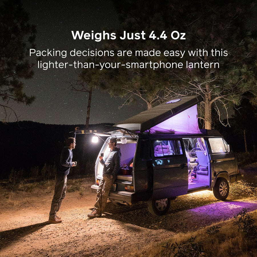Two people standing next to a van with a purple light at night, surrounded by trees.