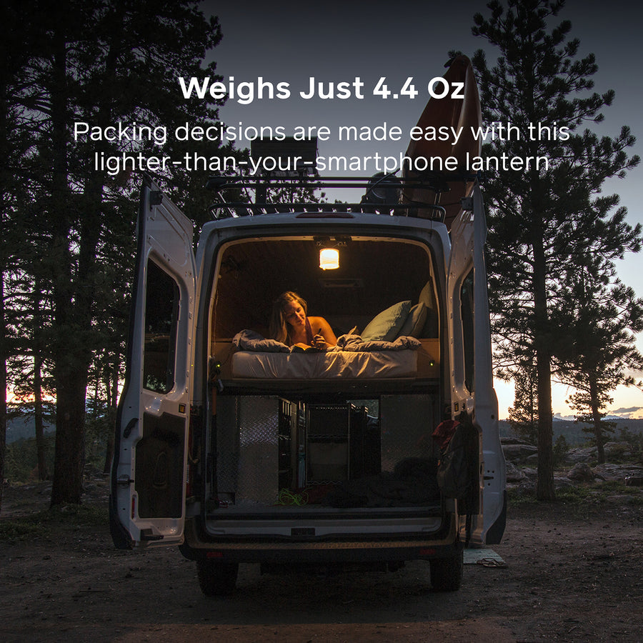 Person inside a van with a lantern, surrounded by trees at dusk.