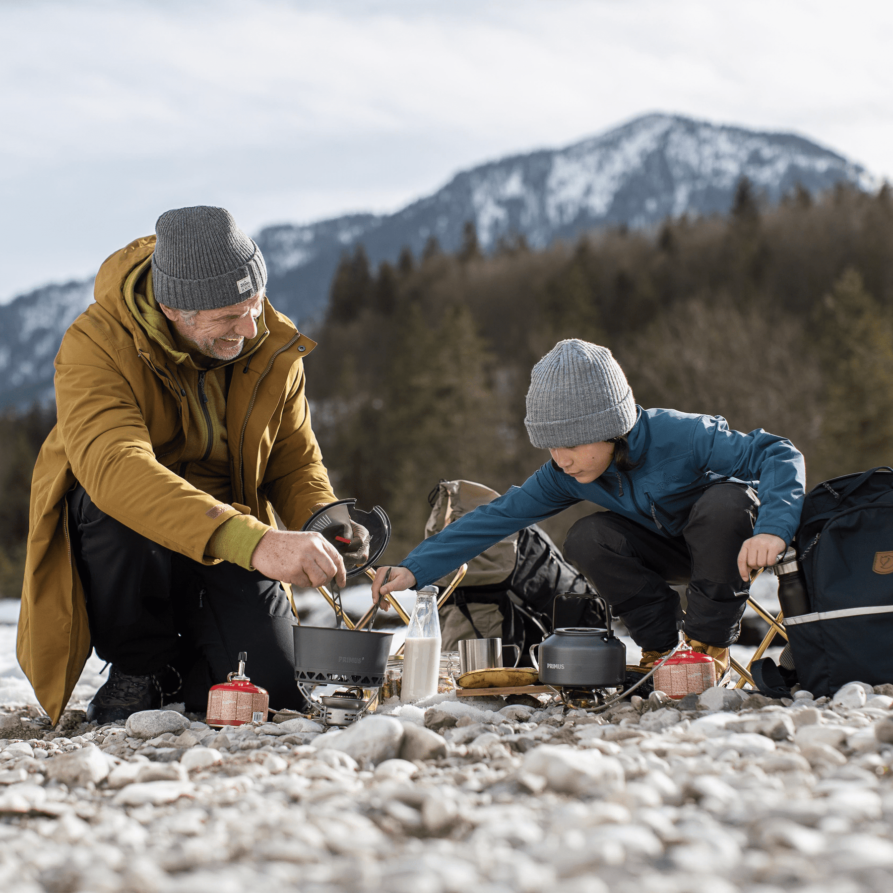 Two people preparing a meal outdoors with mountains in the background