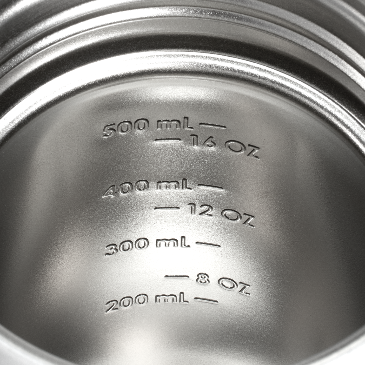 Close-up of a metallic container lid with measurement markings in milliliters and ounces.