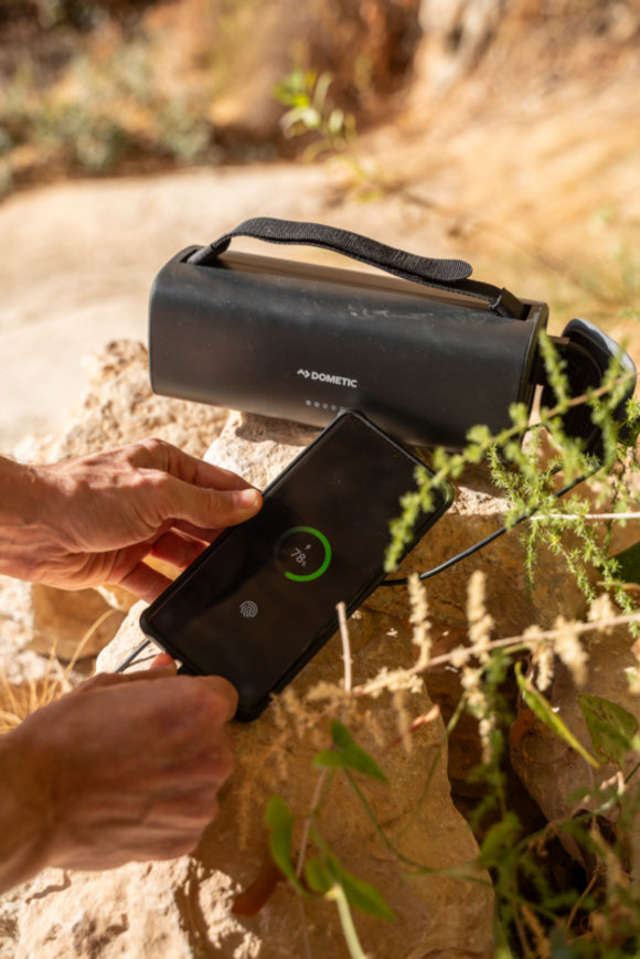 The Dometic PLB15 battery powering portable electronics outdoors, demonstrating its lightweight, ergonomic design for one-day off-grid adventures