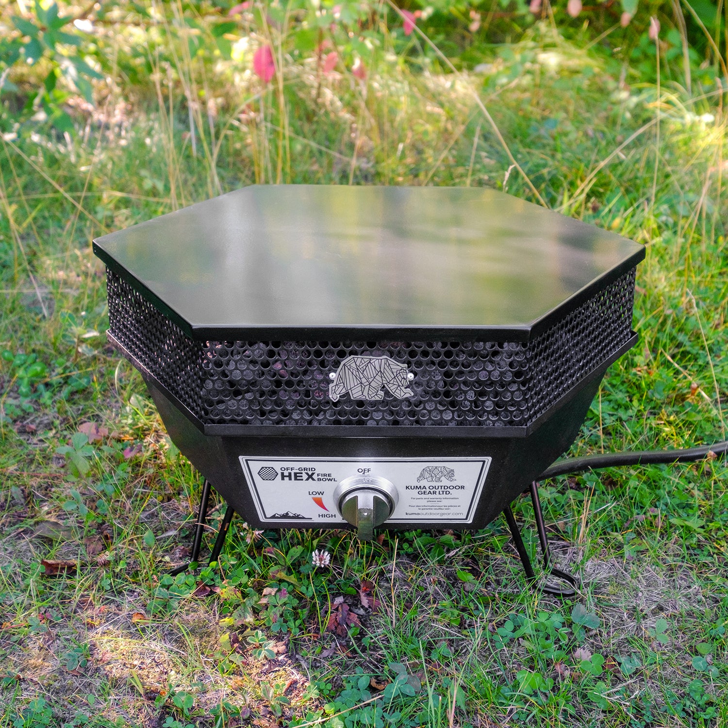 A compact 19-inch hexagonal fire pit with a sleek black finish, featuring three foldable legs and filled with black lava rocks. The fire pit is shown with its lid and strap nearby.