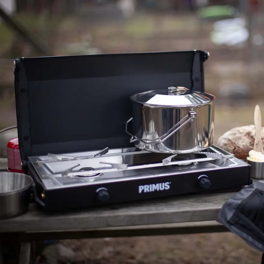 Slim-profile 2-burner camp stove folded with wood-trimmed locking handle for secure transport and storage.