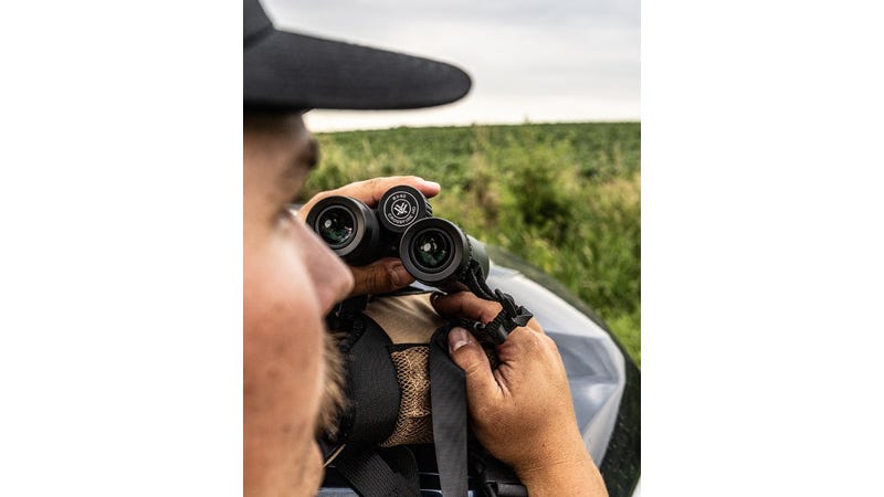 Person holding a pair of binoculars with a natural outdoor setting in the background