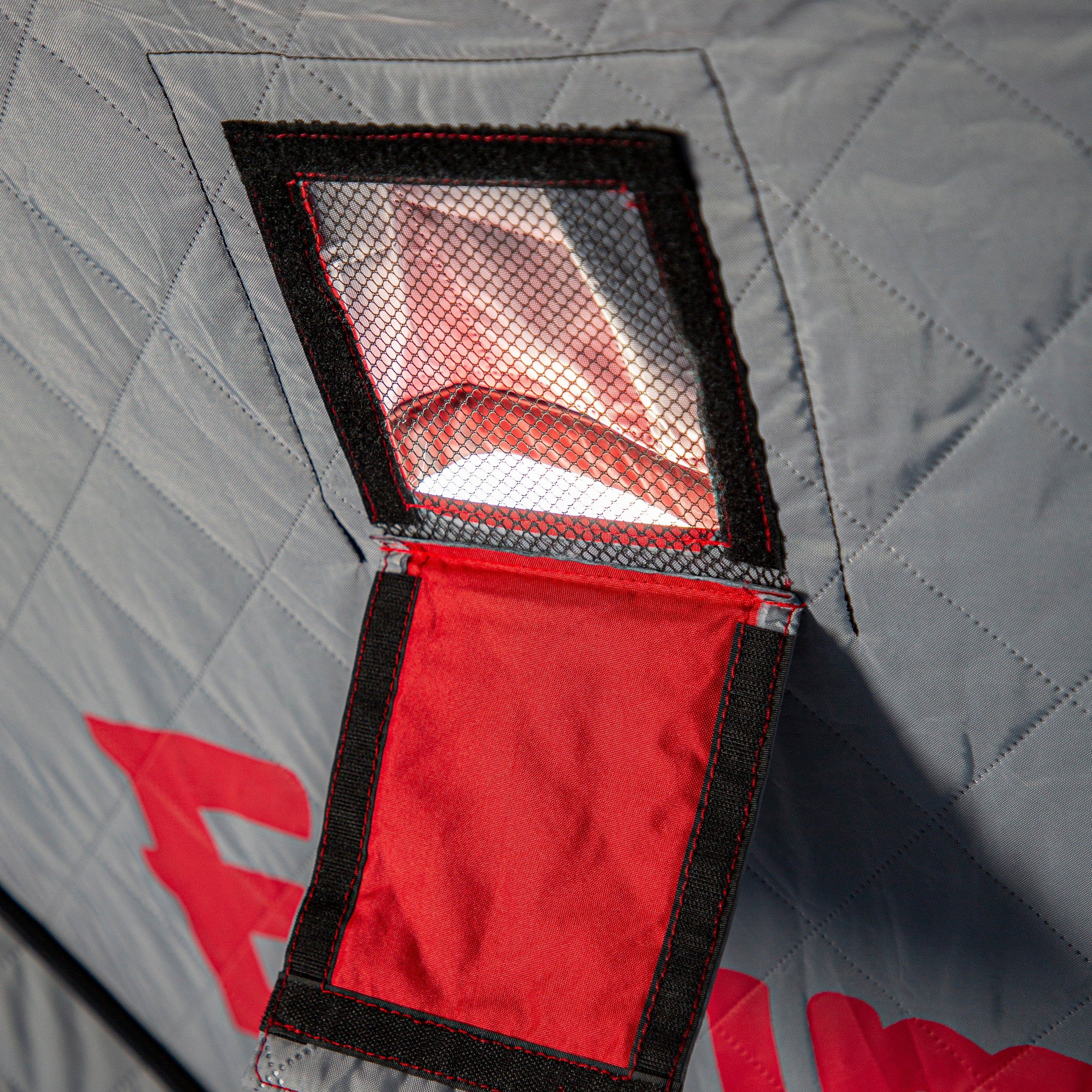 Red interior of a car seat with a quilted gray cover in the background