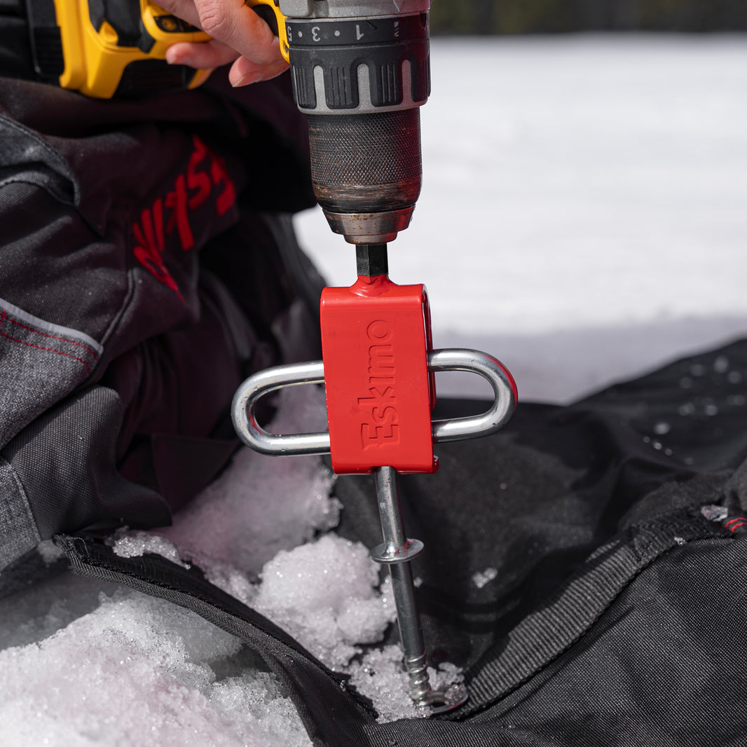 Person using a drill with a red Eskimo ice fishing tool in the snow.