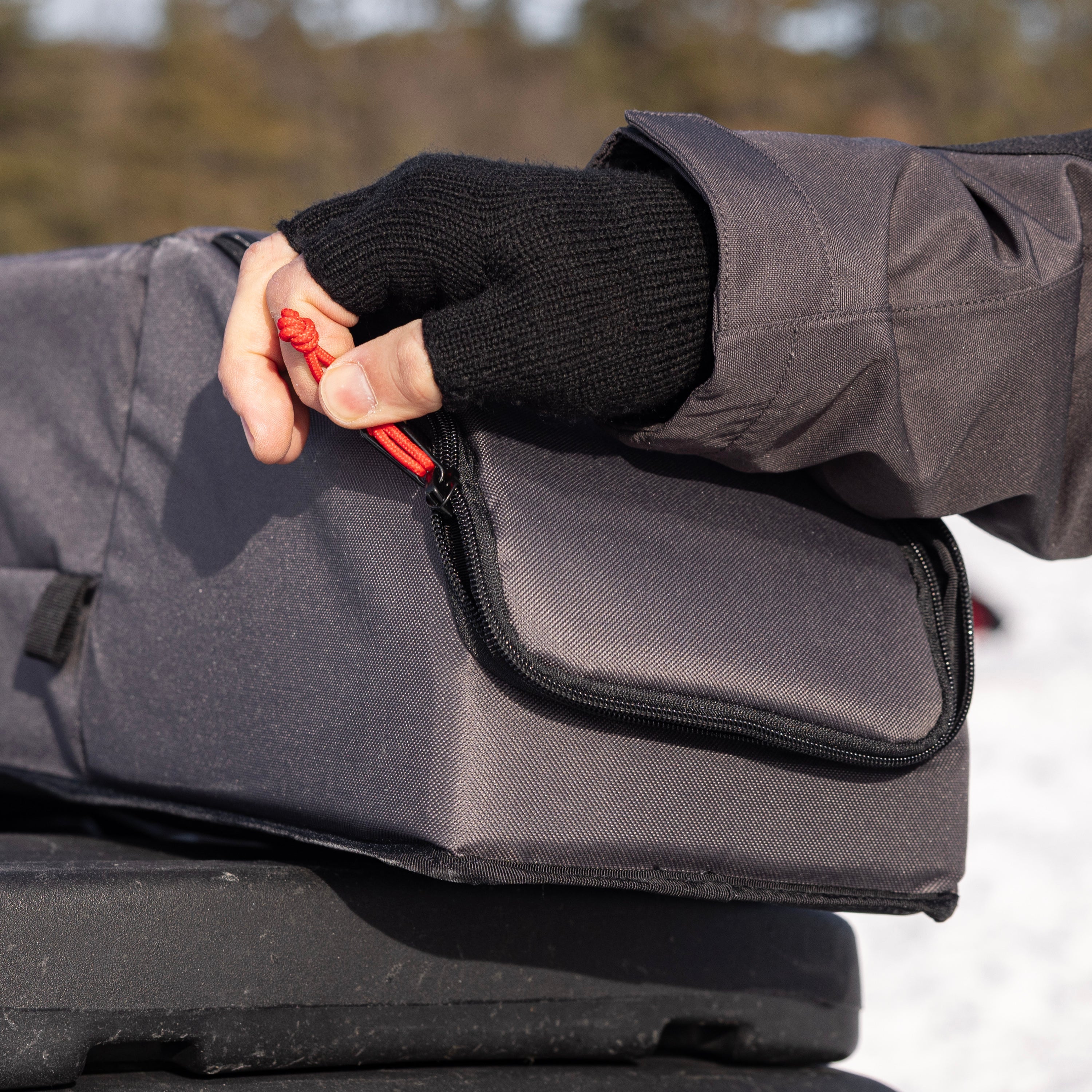 Person wearing black gloves and a gray jacket holding a red tool over a black bag.