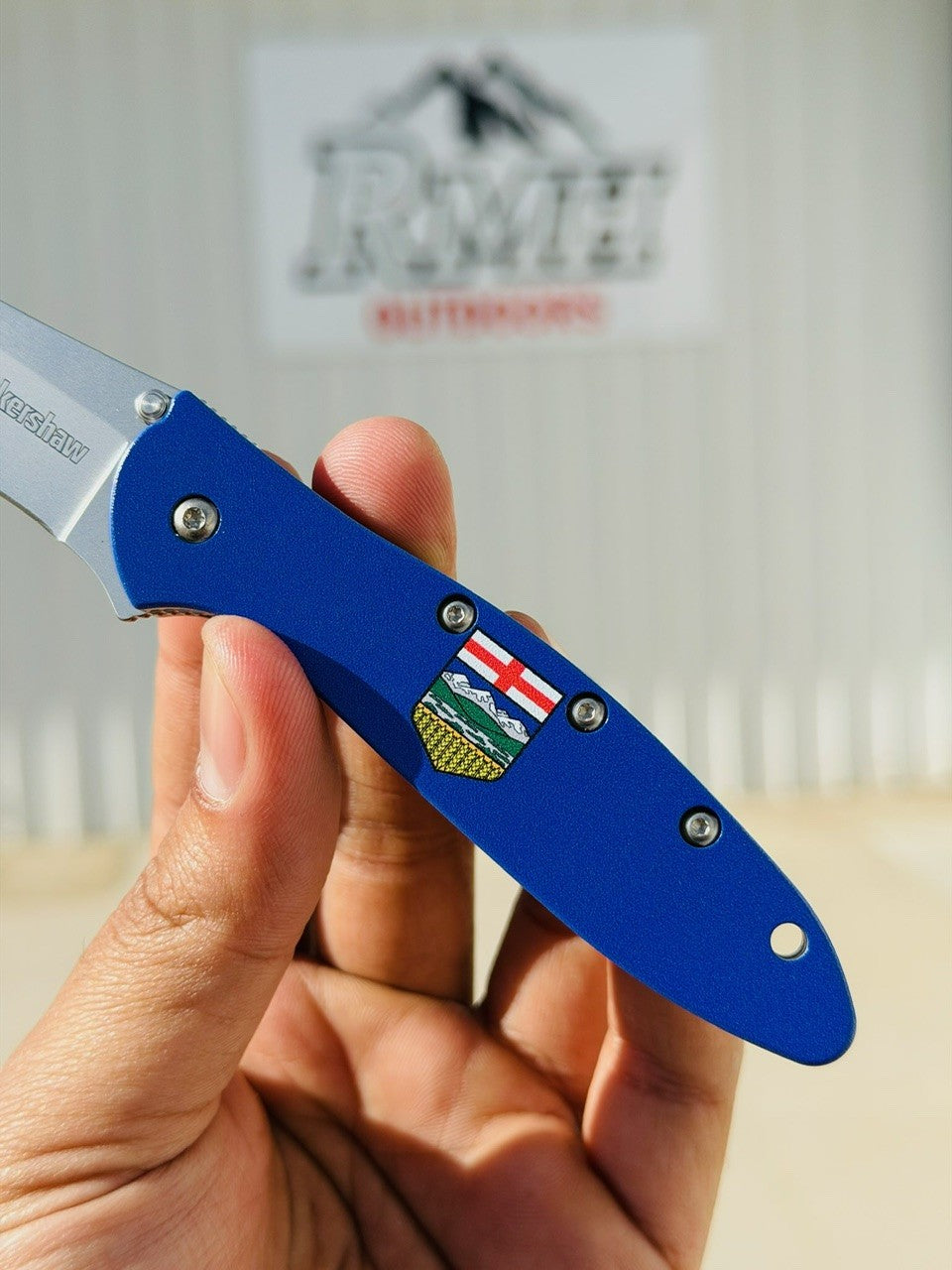 Blue folding knife with a visible brand logo held by a hand, blurred background