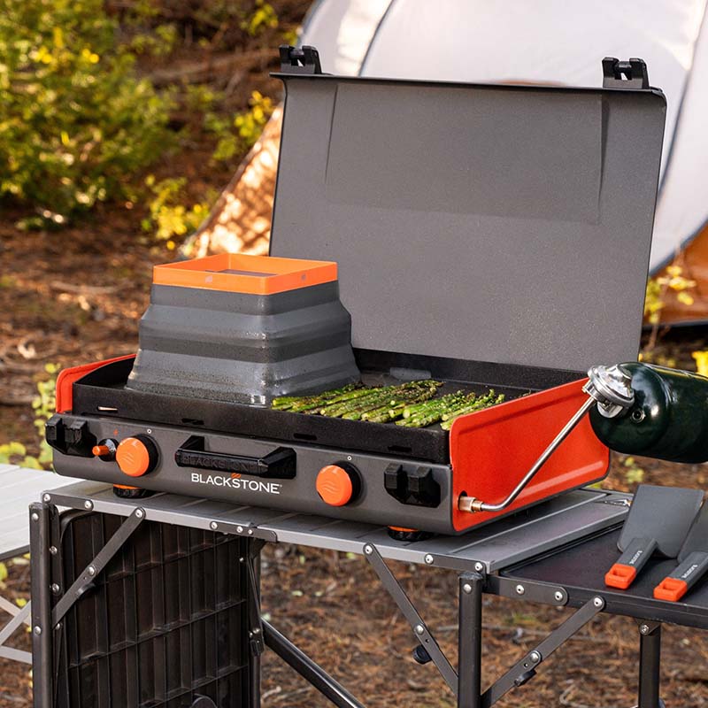 The Blackstone Camping Griddle with its hood lifted, revealing a 20”x14” ceramic titanium-coated griddle top. The cooking surface is spacious, offering 280 sq. in. with dual heat zones.

