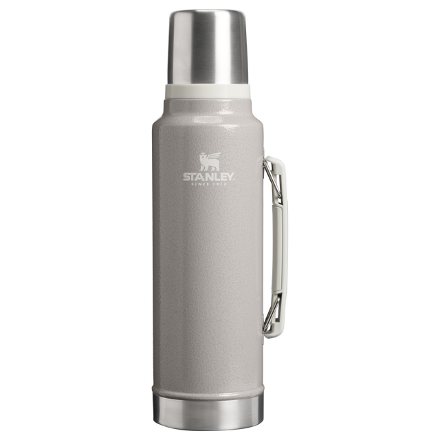 A Stanley vacuum-insulated water bottle with a textured light gray body, stainless steel cap and base, and a metal side handle, shown on a plain white background.