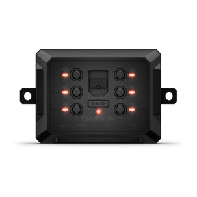 A compact, rugged black box with a sleek, minimalistic design, measuring approximately 4.9 inches in width, 1.3 inches in height, and 3 inches in depth. The Garmin PowerSwitch™ digital switch box features six labeled outputs and two hardwire inputs on one side for controlling 12-volt vehicle accessories. Its surface has a smooth finish, and it is designed to be weather-resistant with an IPX7 rating, making it durable for various outdoor condition