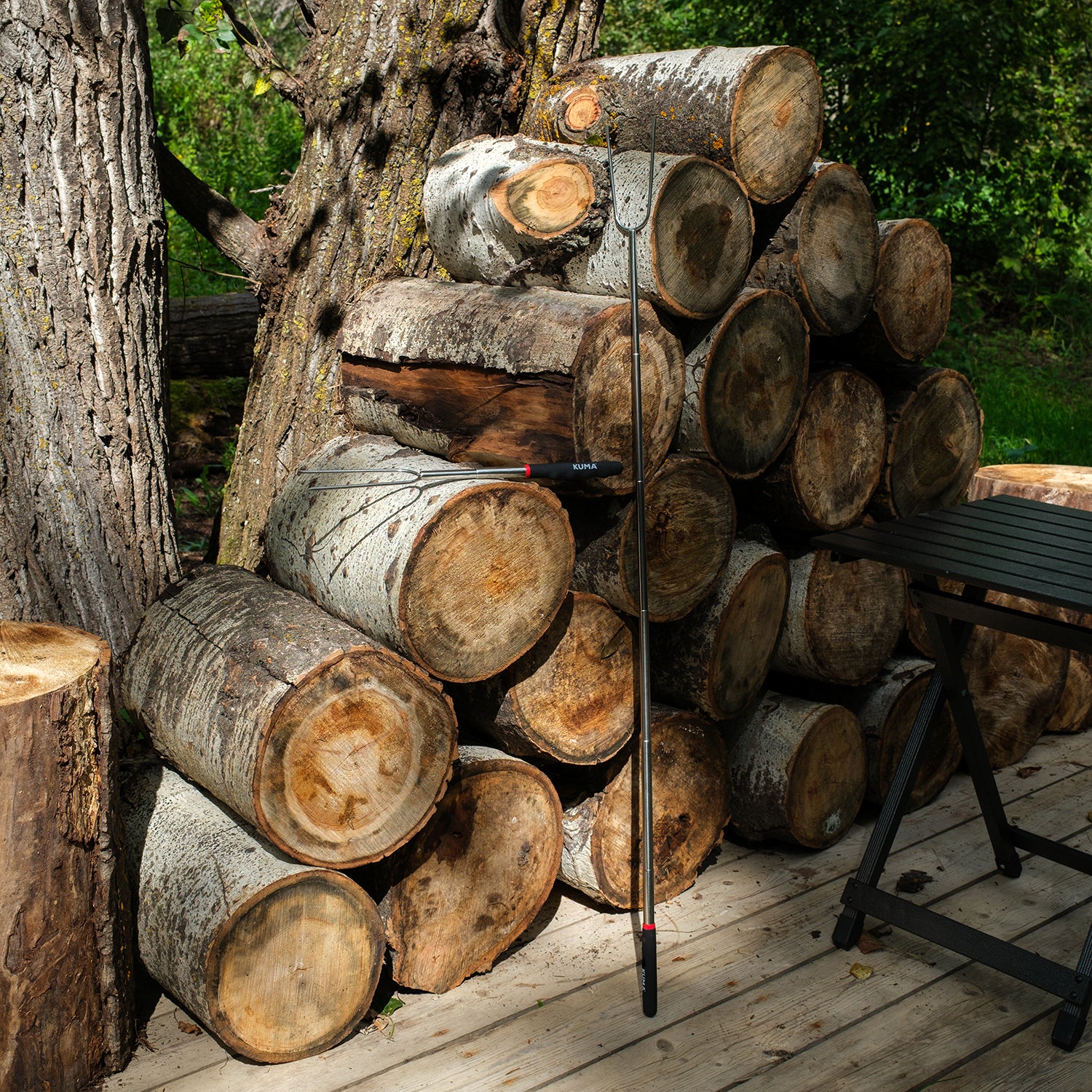 Stack of wooden logs on a wooden deck with a tree in the background